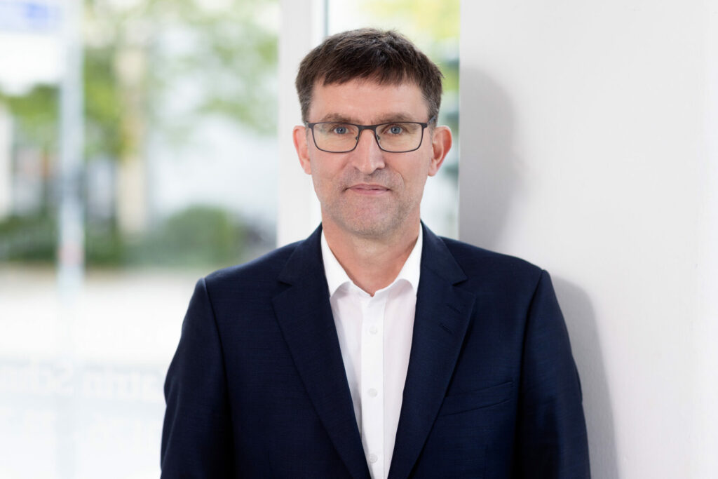Bild von Herrn Niedermöller in einem blauen Anzug vor einem unscharfen Hintergrund.